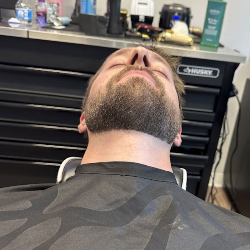 Man reclining in barbershop chair with well-groomed beard, showcasing professional grooming services at Joni's Gentleman's Cuts in Lone Tree, CO.