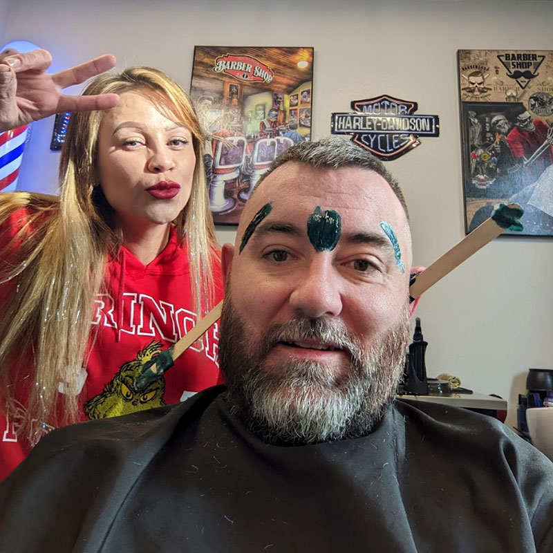 Man getting a grooming service with hair color applied, smiling with a stylist in a barber shop setting, showcasing a relaxed atmosphere for men's grooming.