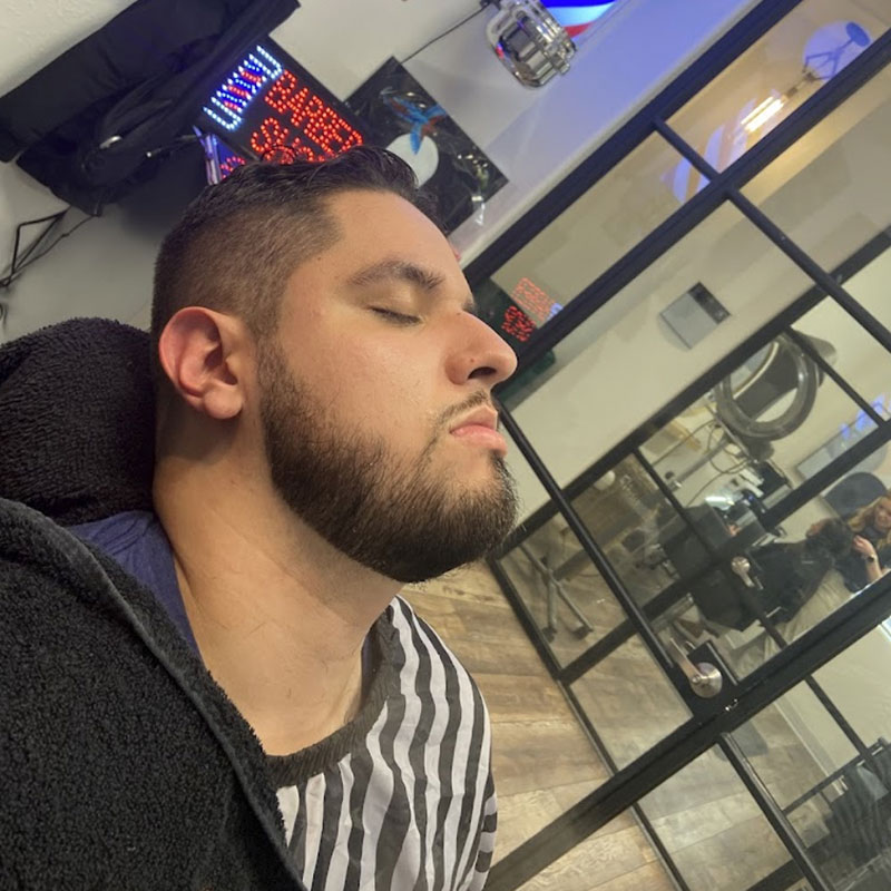 Man relaxing in barber chair with closed eyes, showcasing a stylish haircut and beard, in a modern barber shop setting.