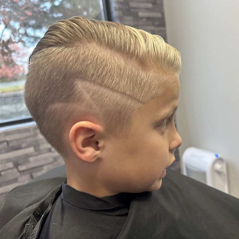 Boy with a stylish undercut hairstyle featuring a clean fade and textured top, showcasing modern barbering techniques in a professional barber shop setting.