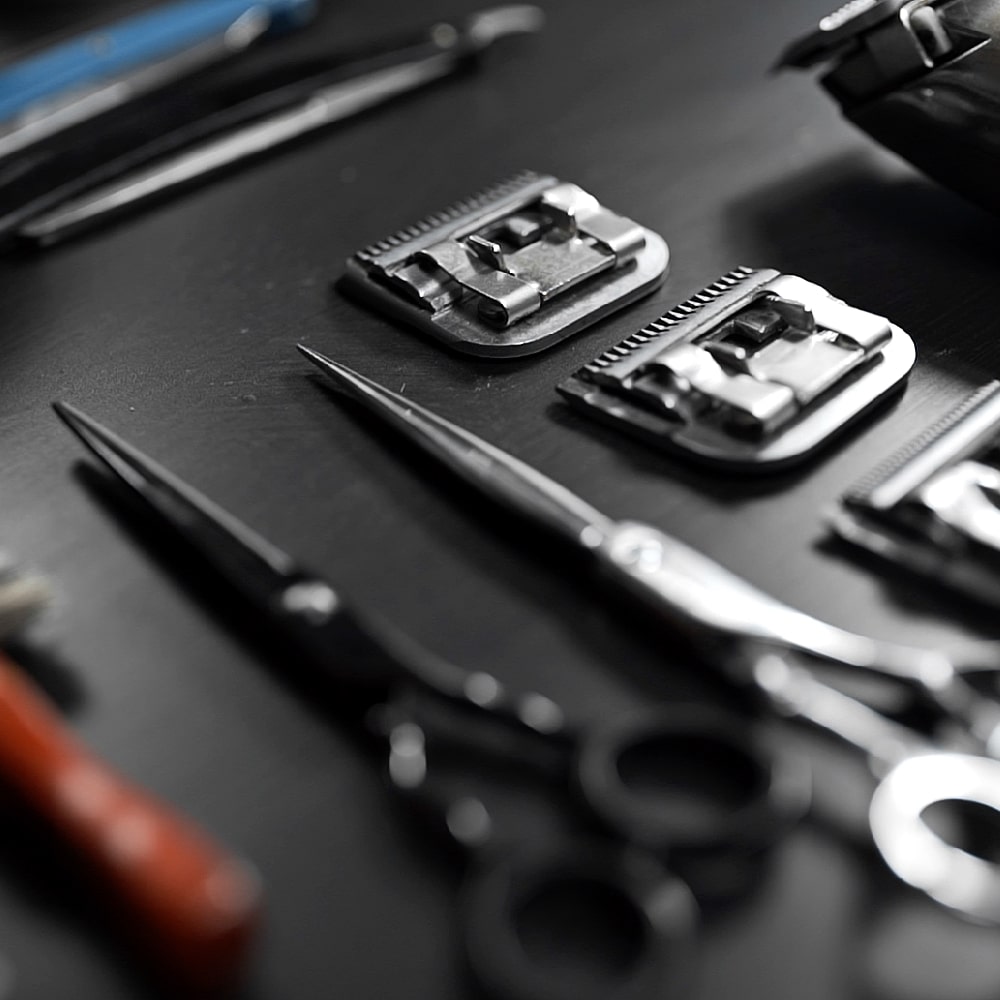 Close-up of sharp professional barbering shears and two metal clipper blades on a dark background.