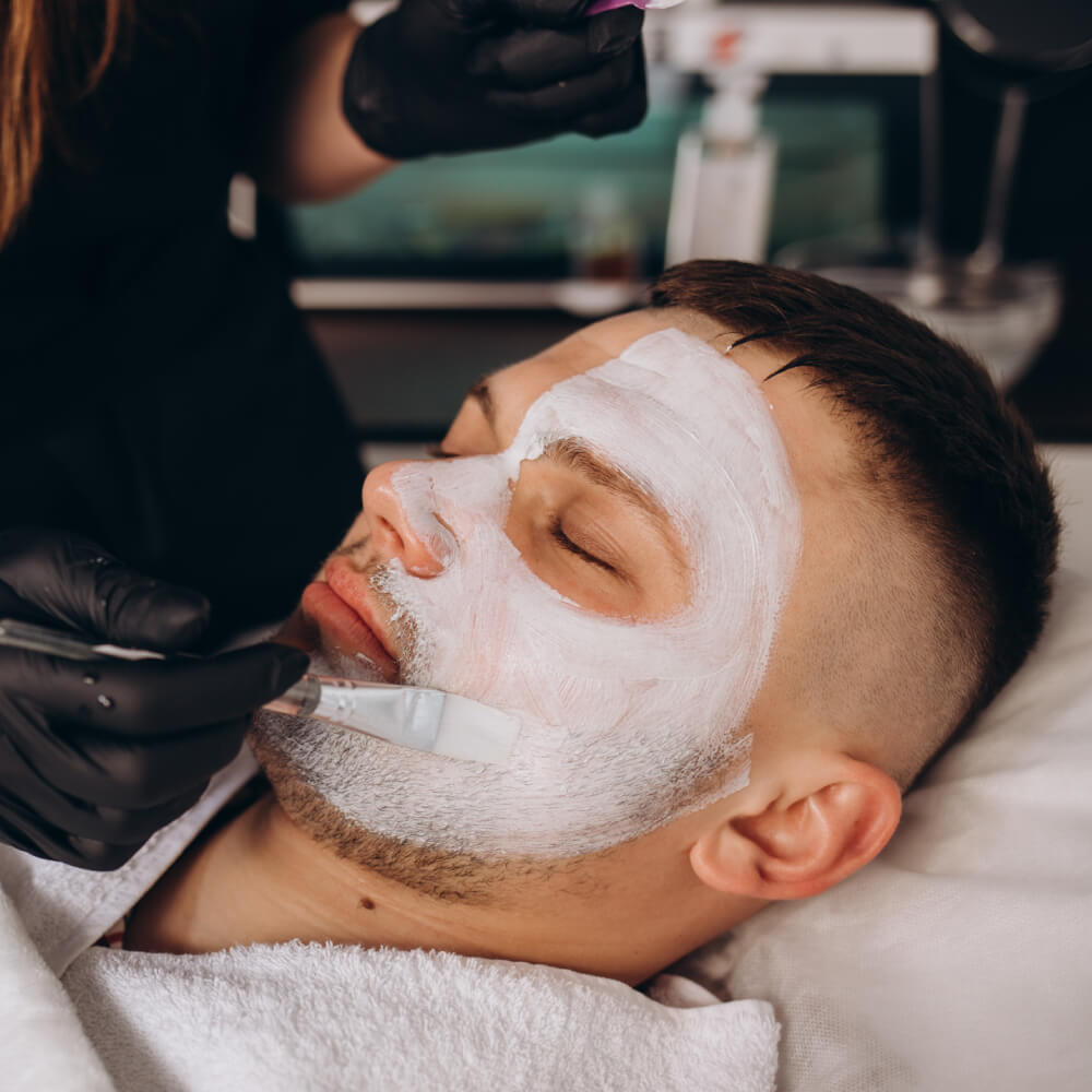 Man relaxing with a white clay face mask being applied during a men's facial treatment
