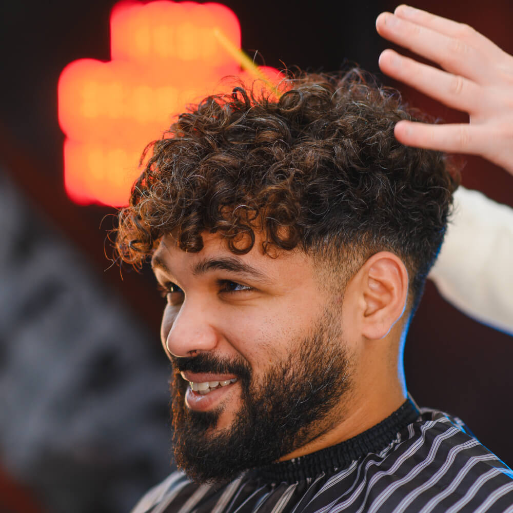 Smiling man with a curly permed men's hairstyle having his hair styled in a barbershop